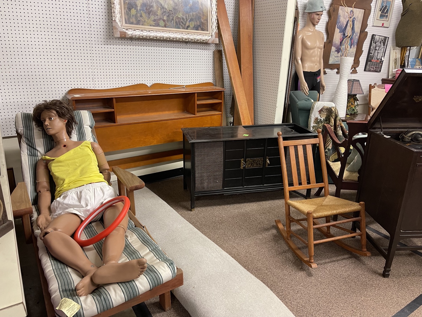 A mannequin lounges with a steering wheel cover while another hides in the background of an antique store