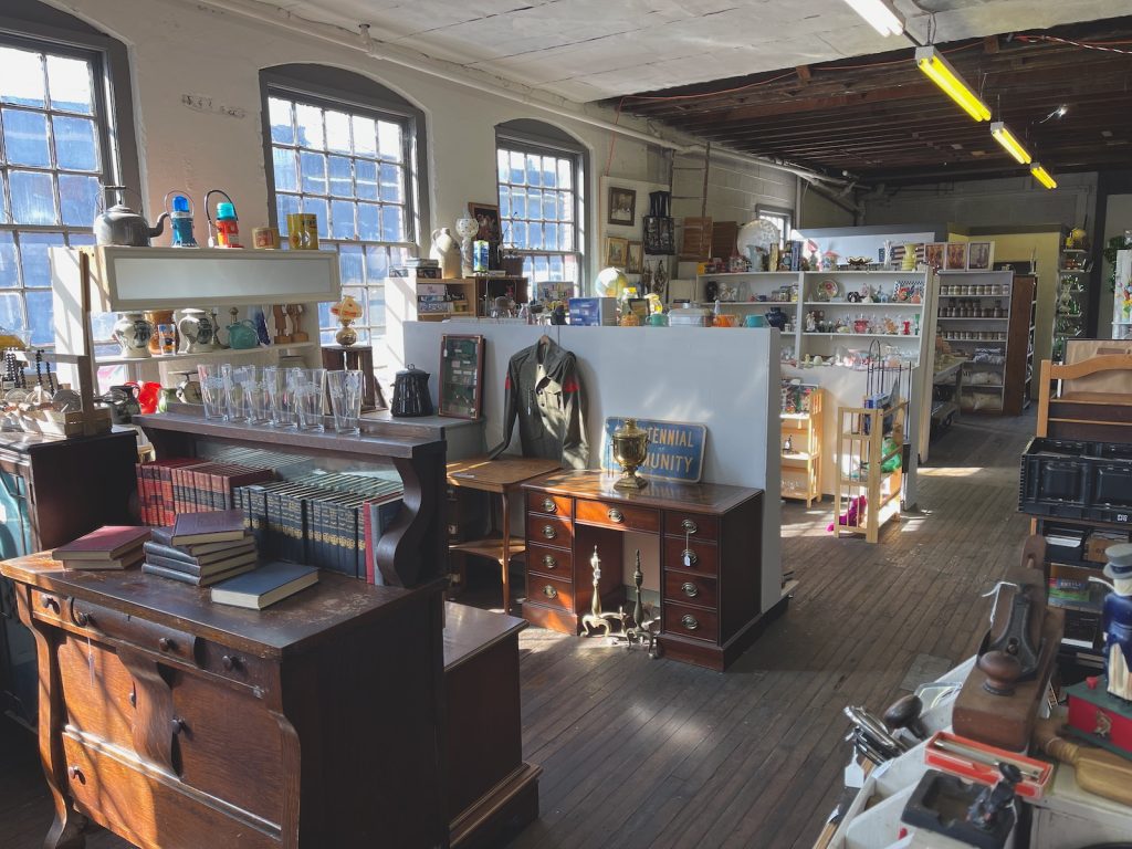Three large windows cast light across many booths of a local antique co-op. Books, glasses, etc.